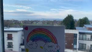 A picture of a rainbow in a window, with the Edinbrugh skyline behind it. 