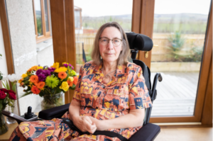 Kate sitting indoors next to windows and vase of flowers