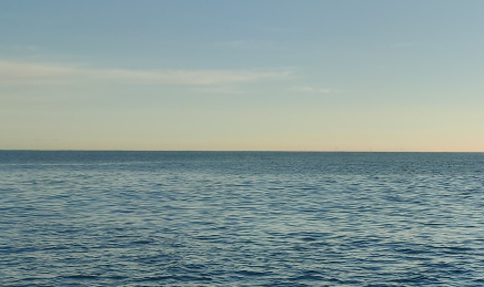 Calm sea waters with a hazy yellowy blue sky in the background