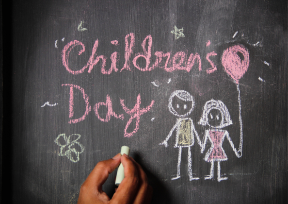 the words "Children's day" and an illustration of two children holding a balloon are chalked onto a blackboard