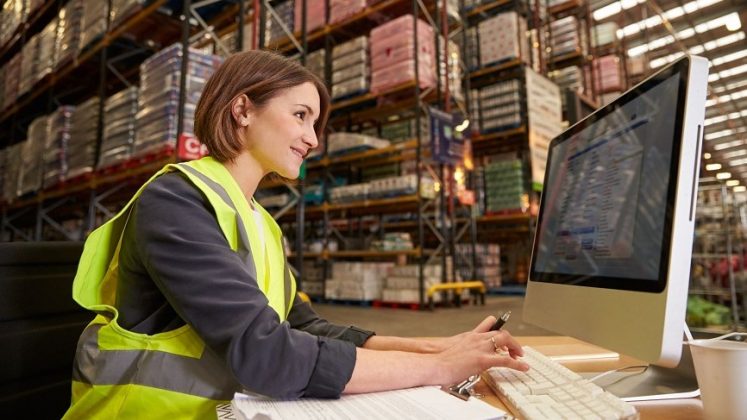 Woman in hi-vis jacket using a computer within a warehouse